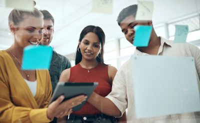 Shot of a group of businesspeople using a digital tablet while brainstorming with notes on a glass wall in an office.